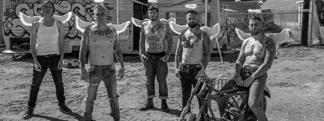 Tattooed Avenged Sevenfold band members with angel wings stand near a motorcycle.