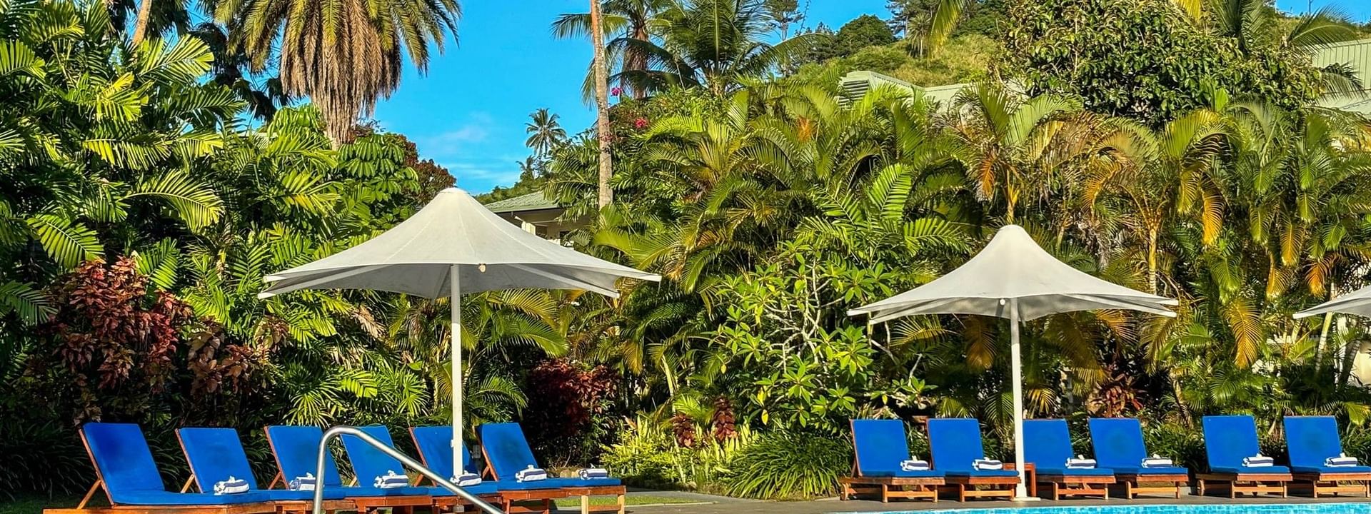 Swimming pool with lounge chairs and umbrellas surrounded by lush vegetation at The Naviti Resort in Korolevu