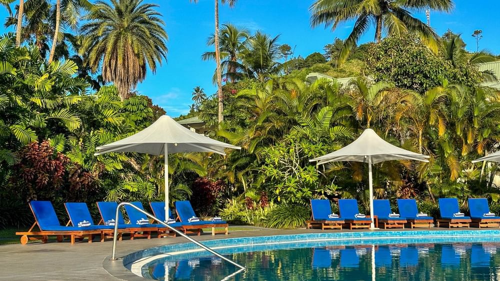 Swimming pool with lounge chairs and umbrellas surrounded by lush vegetation at The Naviti Resort in Korolevu.