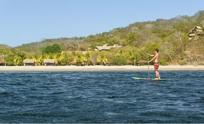 Man paddleboarding on calm water near the private beach at Morgan’s Rock, one of the hotels in San Juan del Sur