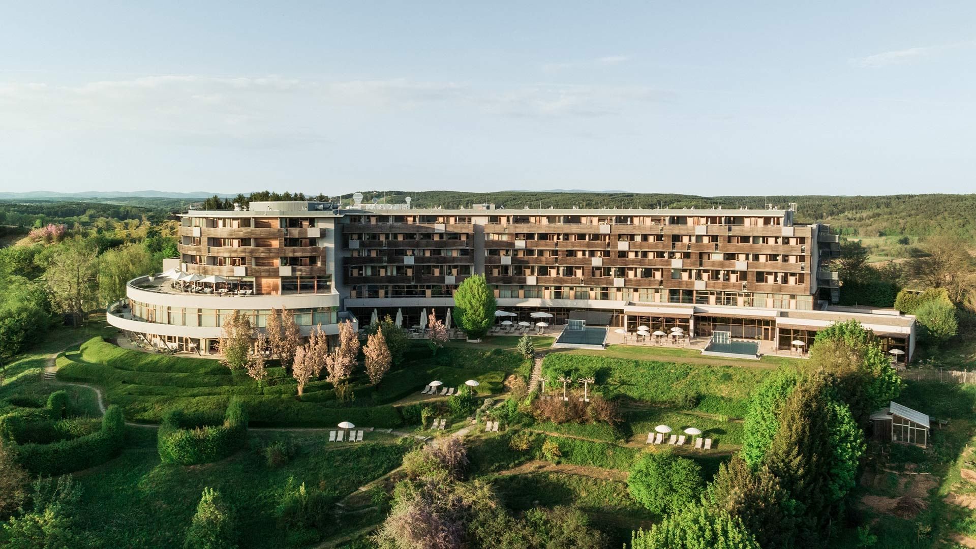 Aerial view of a large resort hotel surrounded by greenery, featuring a circular wing and numerous balconies.