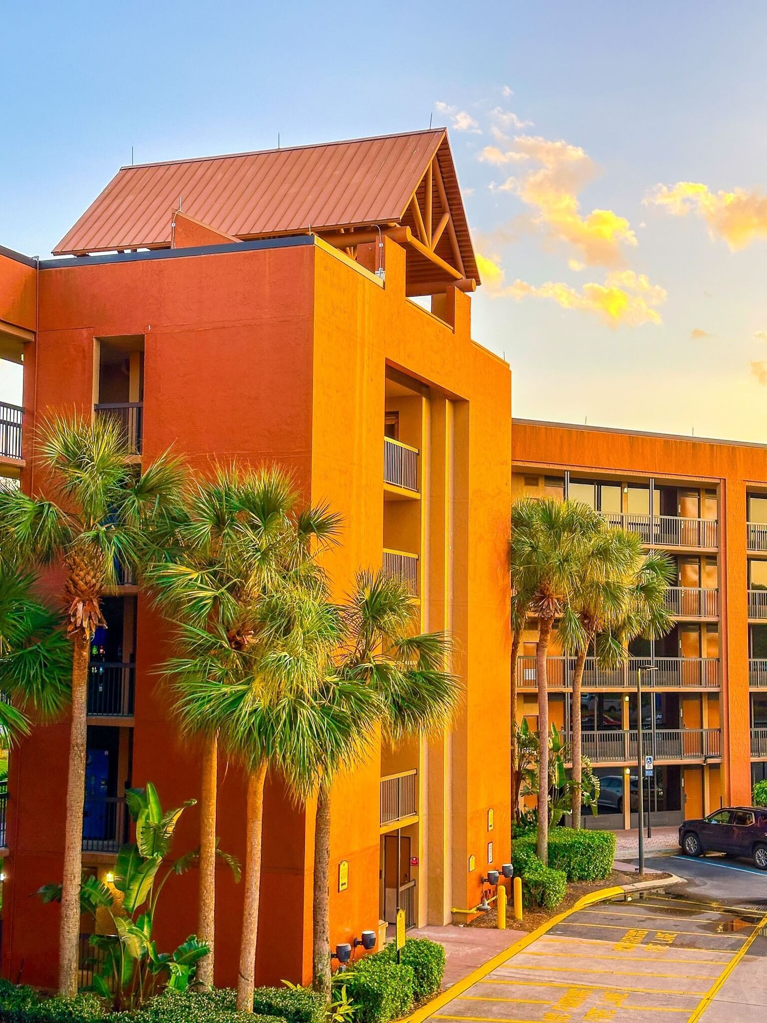 A tall hotel in stucco orang glowing at sunset surrounded by palm trees. Rosen Inn Lake Buena Vista is a great venue for hosting a teen party in Orlando.