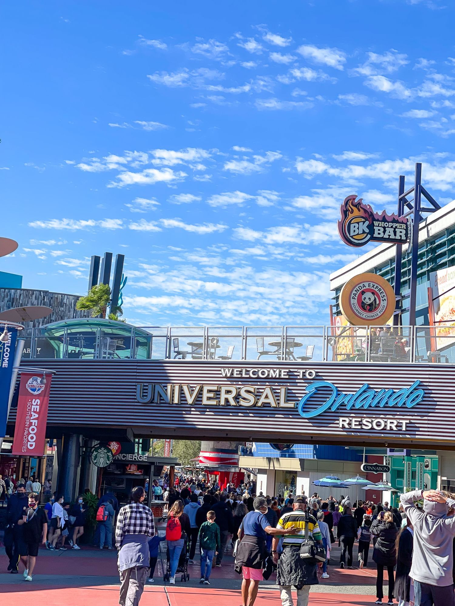 A walkway with a sign that reads "Universal Orlando Resort" surrounded by crowds of people and signs for restaurants. This is the Universal Orlando CityWalk.