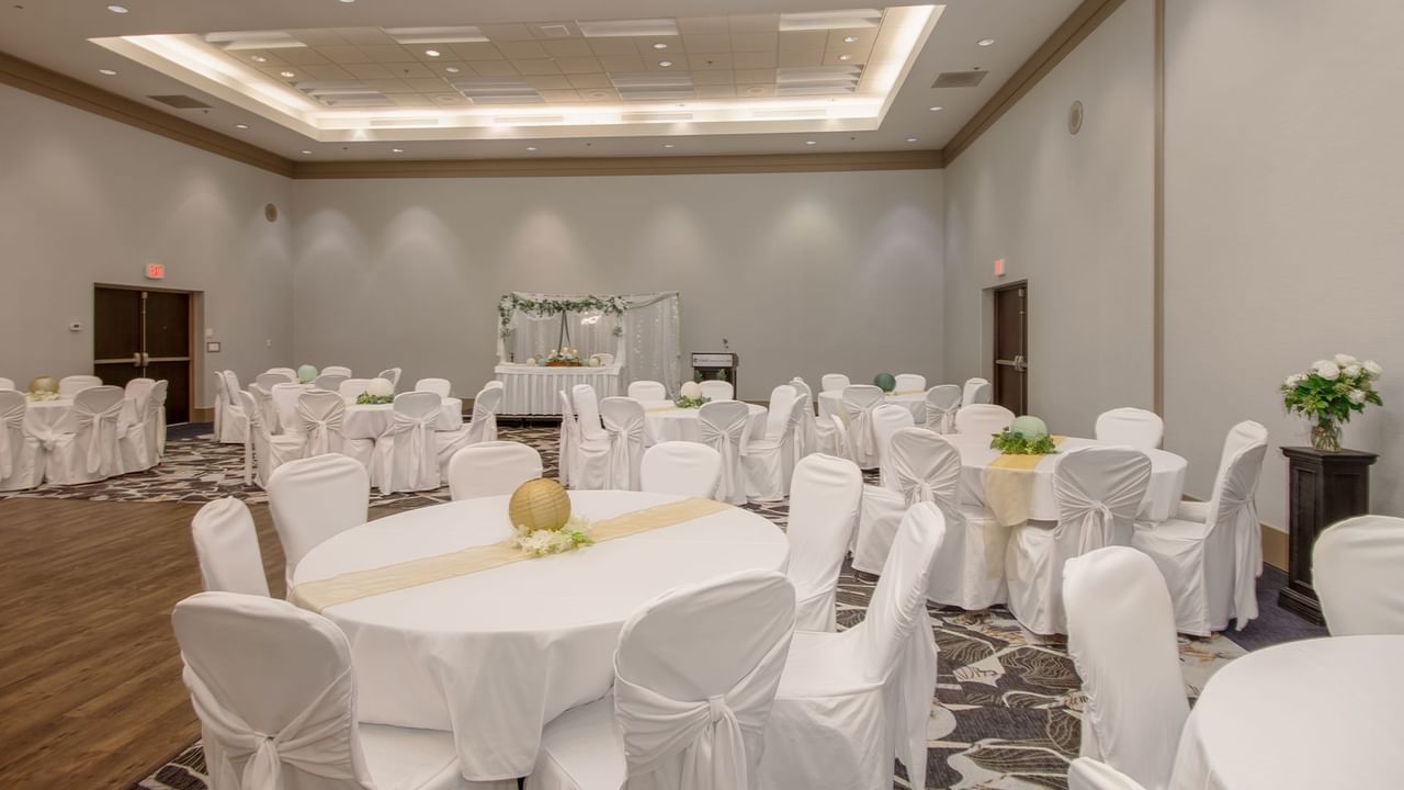 A large room with round tables covered in white cloth, chairs, and a decorated stage.