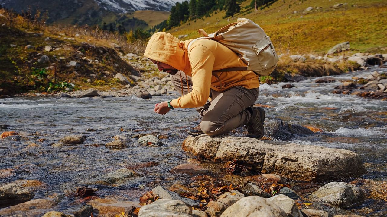 traveler in a yellow hoodie knealing beside a river