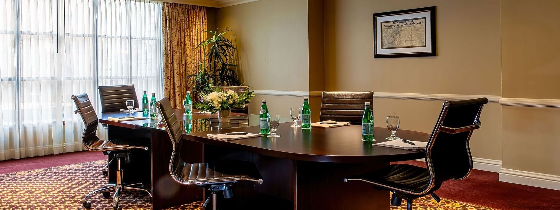Black rolling chairs by a conference table under soft lights near a tall plant in Centennial at Warwick Denver
