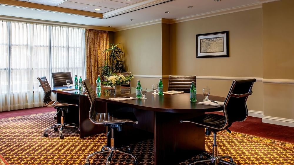 Black rolling chairs by a conference table under soft lights near a tall plant in Centennial at Warwick Denver