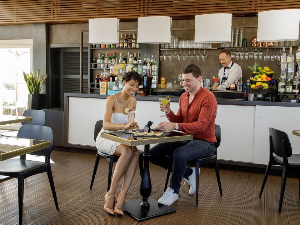 Couple enjoying drinks and sushi platter at Terrazza Cielo with bar in the background at The Independent
