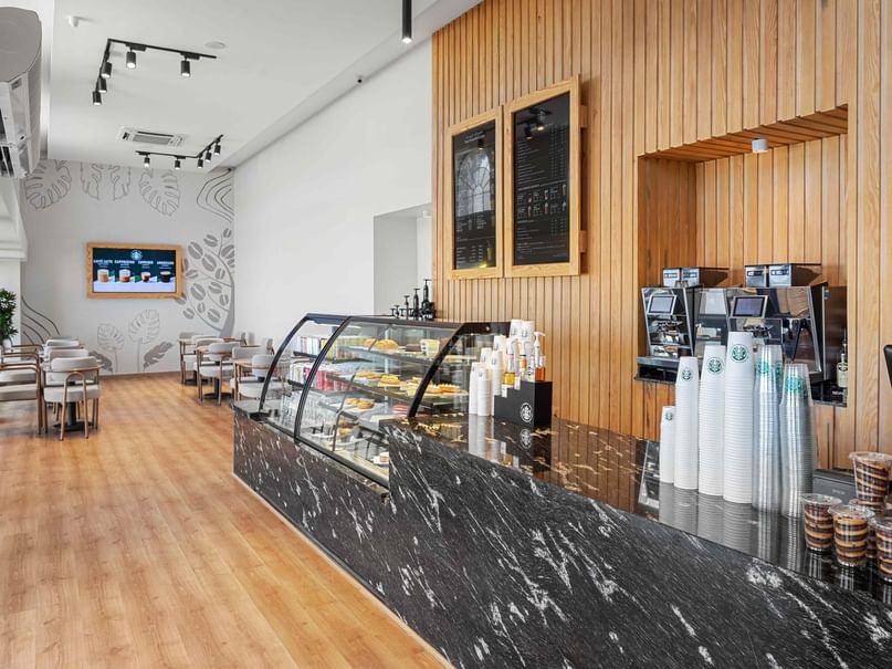 Modern coffee shop interior with wooden floors, black marble counter, and seating area, featuring a display case and coffee cups.