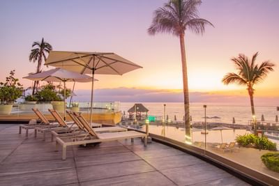 Parte de las instalaciones exteriores del hotel Sunset Plaza Beach Resort, con tumbonas, sombrillas, piscina, plantas y vistas a la playa en Puerto Vallarta