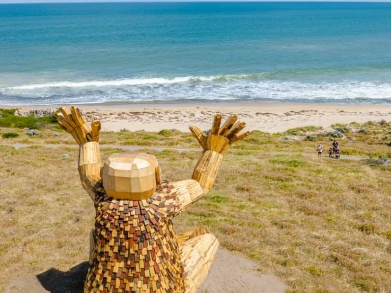 Large wooden statue with its hands raised towards the sky, overlooks the ocean near The Sebel Mandurah
