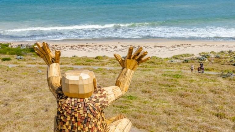 Large wooden statue with its hands raised towards the sky, overlooks the ocean near The Sebel Mandurah