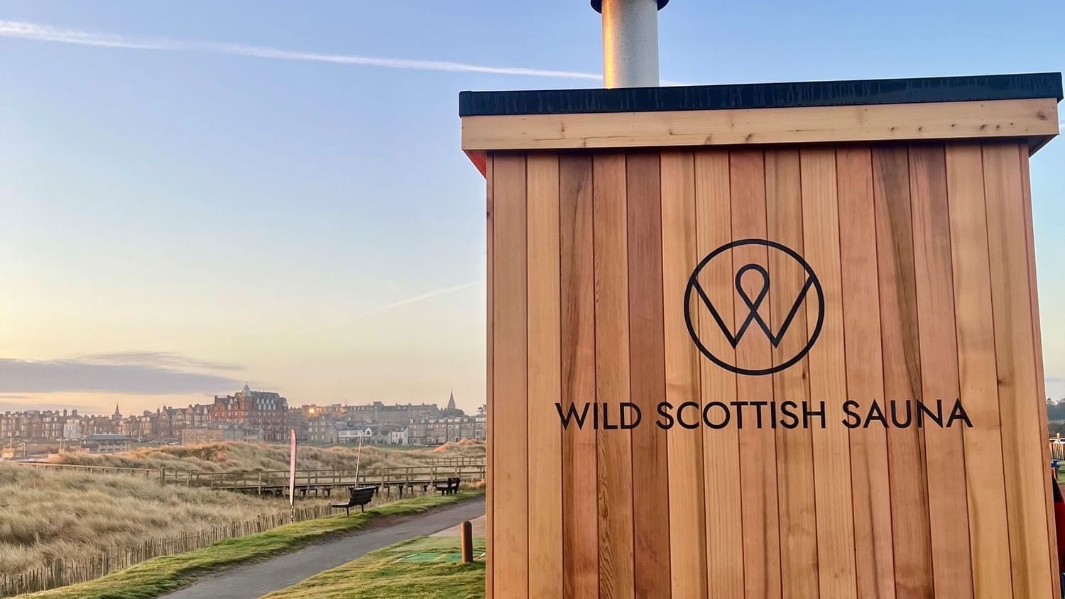 Close-up of a wooden sauna hut with a logo, captured at sunset near Seaton House
