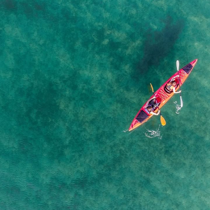 Vista aerea di un kayak rosso con due persone che remano in acque verdi.