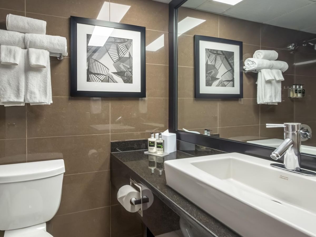 Modern bathroom with brown tile, white fixtures, and framed artwork at Coast Calgary University Area Hotel by APA