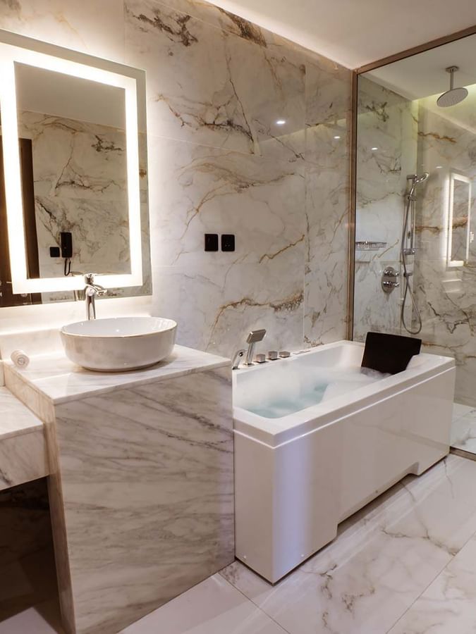 Marble bathroom featuring a white bathtub by a glass shower in Ambassador Suite at Cantonal Hotel by Warwick Riyadh
