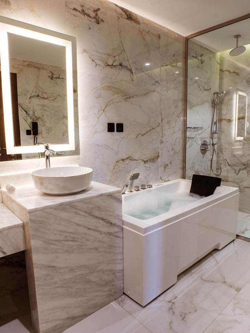 Marble bathroom featuring a white bathtub by a glass shower in Ambassador Suite at Cantonal Hotel by Warwick Riyadh
