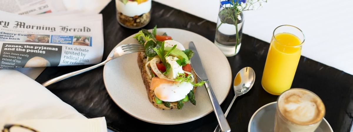 In-room breakfast setup with coffee, juice, newspaper, and a healthy meal at Novotel Sydney International Airport