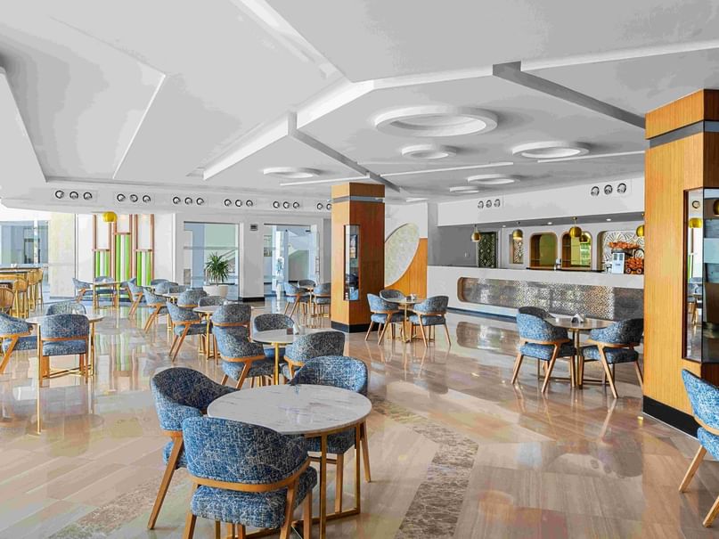 Interior of an elegant Cappuccino Bar with multiple tables, blue chairs, and a patterned floor under a circular-designed ceiling.
