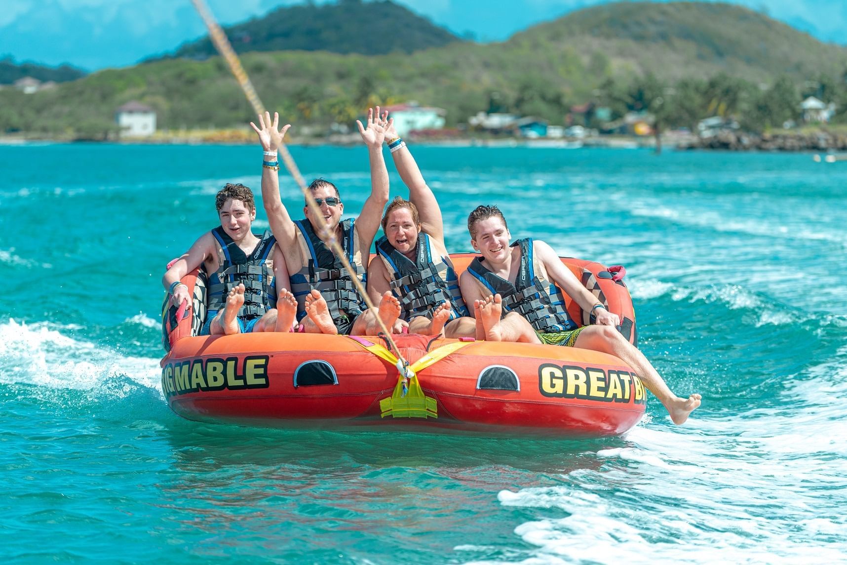 Group of four people joyfully riding a vibrant inflatable banana boat in the sea near Bay Gardens Beach Resort & Spa