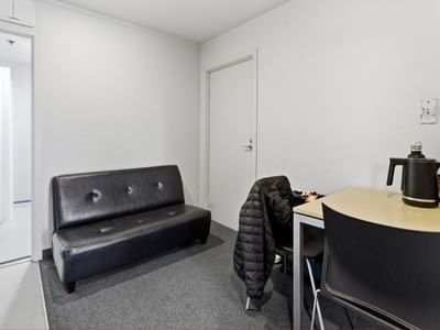 Black couch, table, and chairs in a white room at UniLodge Stafford House.