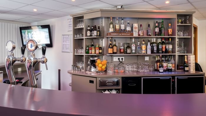 Bar counter with alcohol bottle shelves at The Originals Hotels