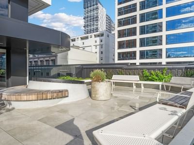 Modern rooftop terrace with white lounge chairs, planters, and city views at UniLodge Auckland Central