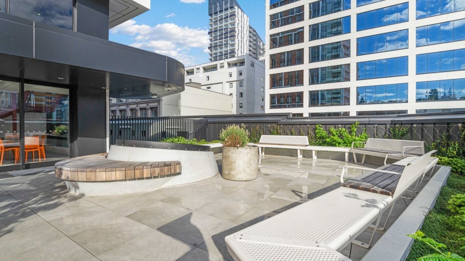 Modern rooftop terrace with white lounge chairs, planters, and city views at UniLodge Auckland Central