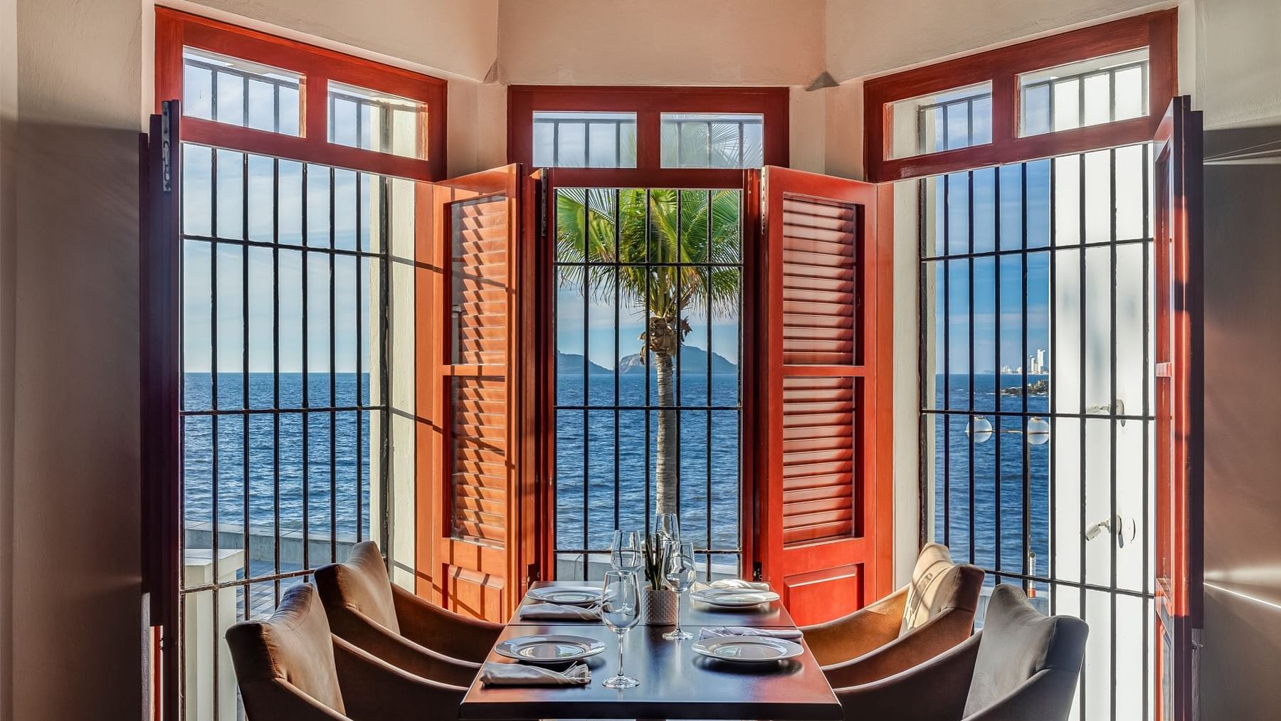 Elegant restaurant dining area with tables set and a panoramic view of the ocean at Curamoria Collection