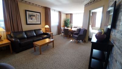 Living & dining areas with leather sofa, near a table and armchairs, in Executive Suite at Glenmore Inn & Convention Centre