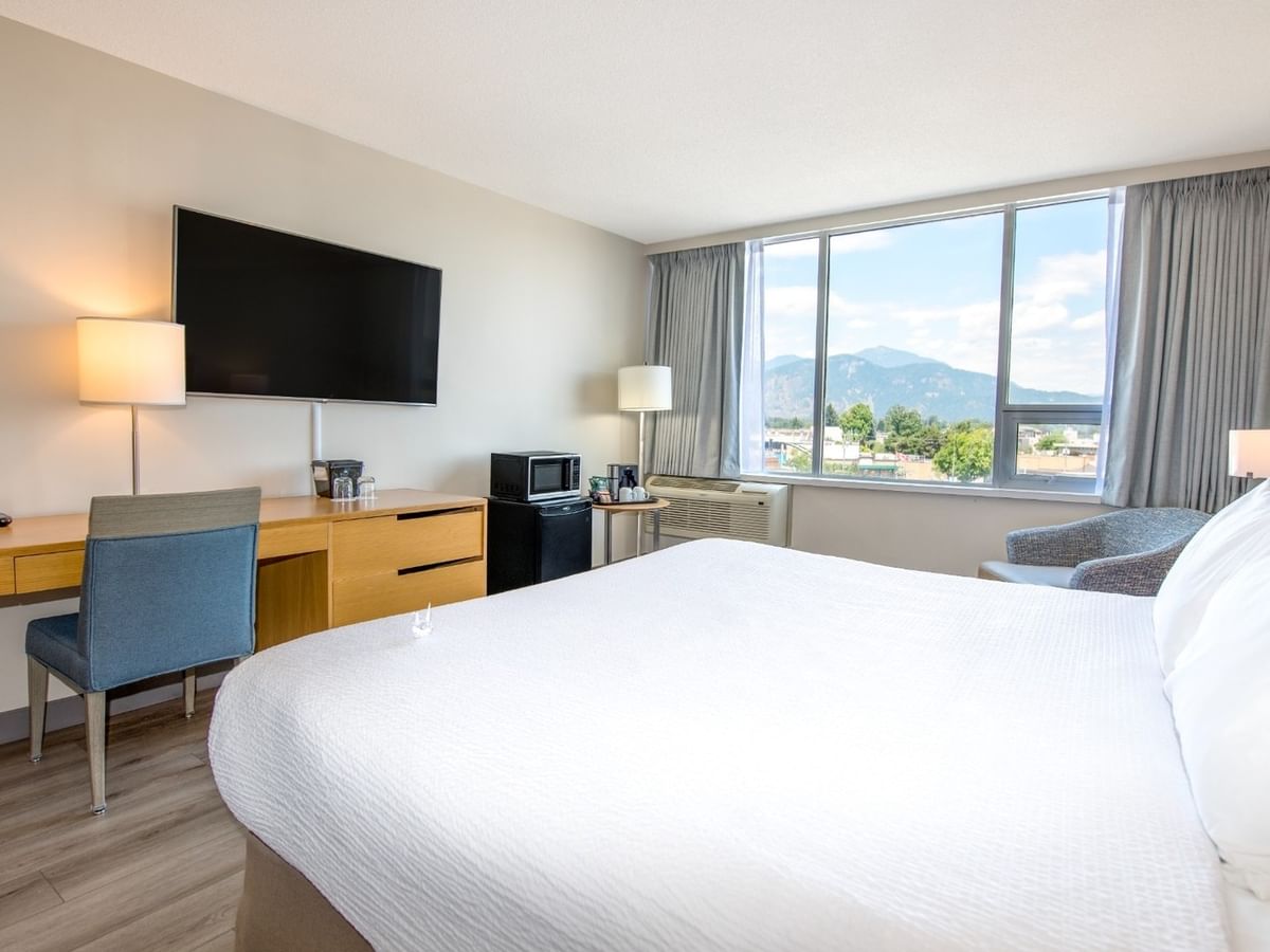 Hotel room with large king bed, work desk, chairs, TV and large window with city view.