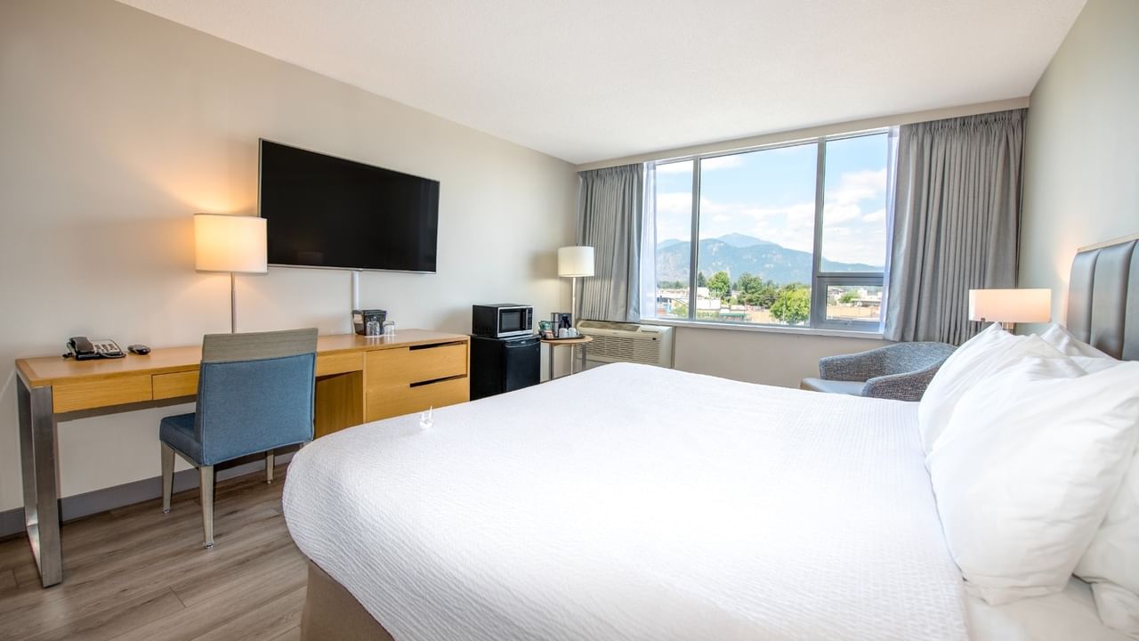 Hotel room with large king bed, work desk, chairs, TV and large window with city view.