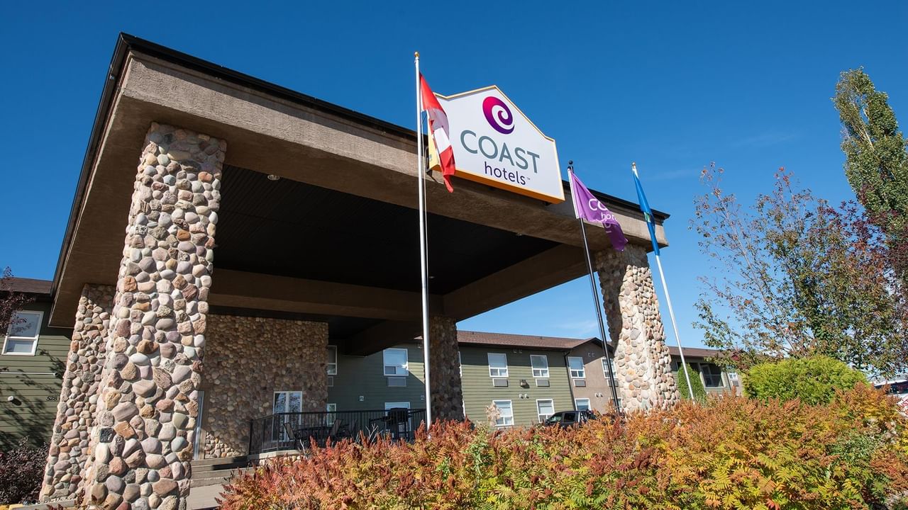 Stone-pillared entrance with Coast Hotels signage and Canadian flag under clear blue sky at Coast Edson Hotel.