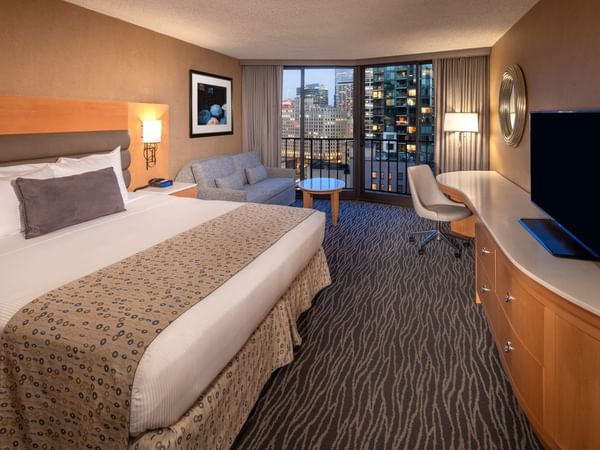 Hotel room with bed, couch, desk, chair, TV, and balcony with city view.