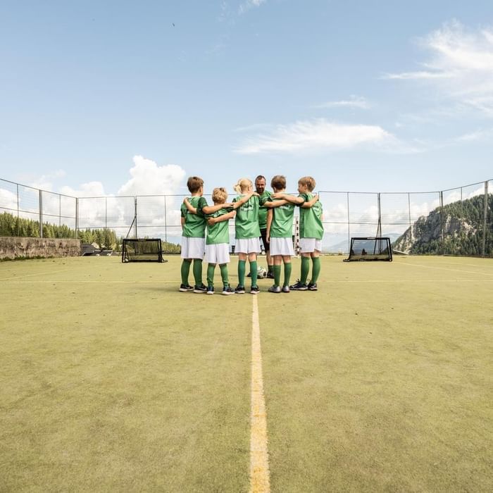 Young soccer team in green uniforms huddles on a field with coach at Falkensteiner Resort Lake Garda
