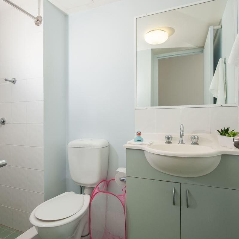 Clean modern bathroom with white toilet, mint green vanity, wall mirror, and tiled flooring at UniLodge on Margaret.