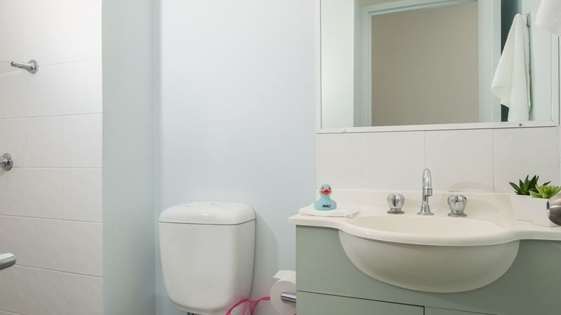 Clean modern bathroom with white toilet, mint green vanity, wall mirror, and tiled flooring at StudentLiving - on Margaret