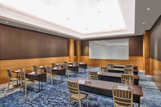 Professional conference room with rows of tables, gold chairs, & a large projection screen in M Floor at Vasa Hotel Surabaya
