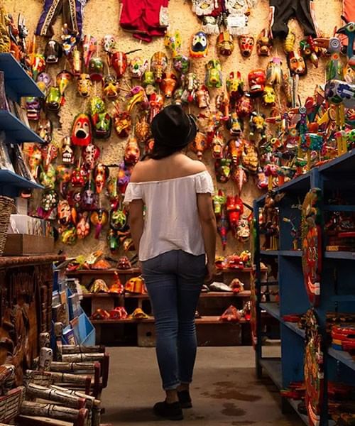 Mujer caminando por una tienda rodeada de máscaras tradicionales en paredes y estanterías de madera en Porta Hotels