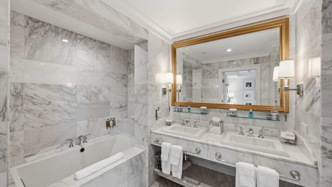 Luxurious Penthouse bathroom with marble walls, dual sinks, soaking tub, and gold-framed mirror at el PRADO Hotel