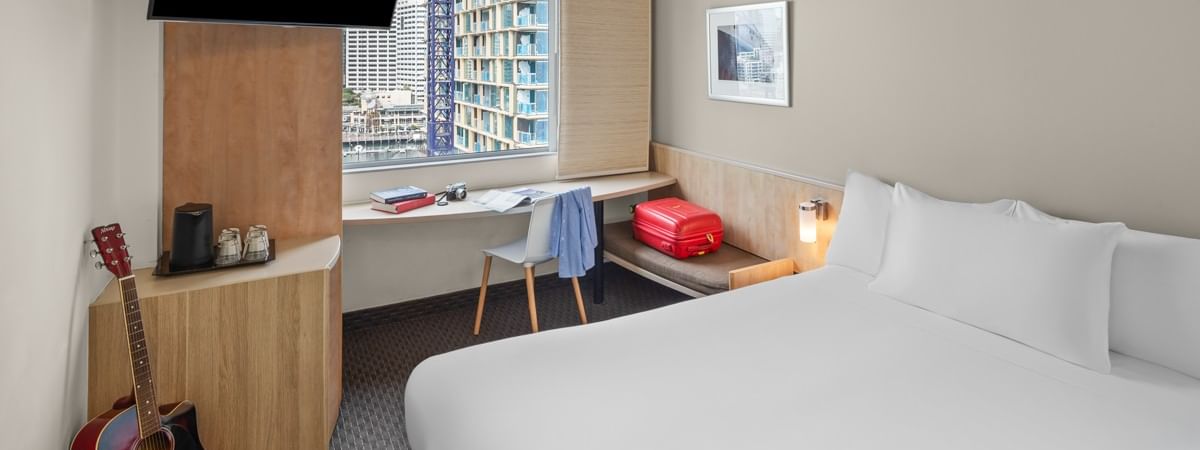 Superior room with one queen bed, desk, wall-mounted TV, and city skyline view at Ibis Sydney Darling Harbour