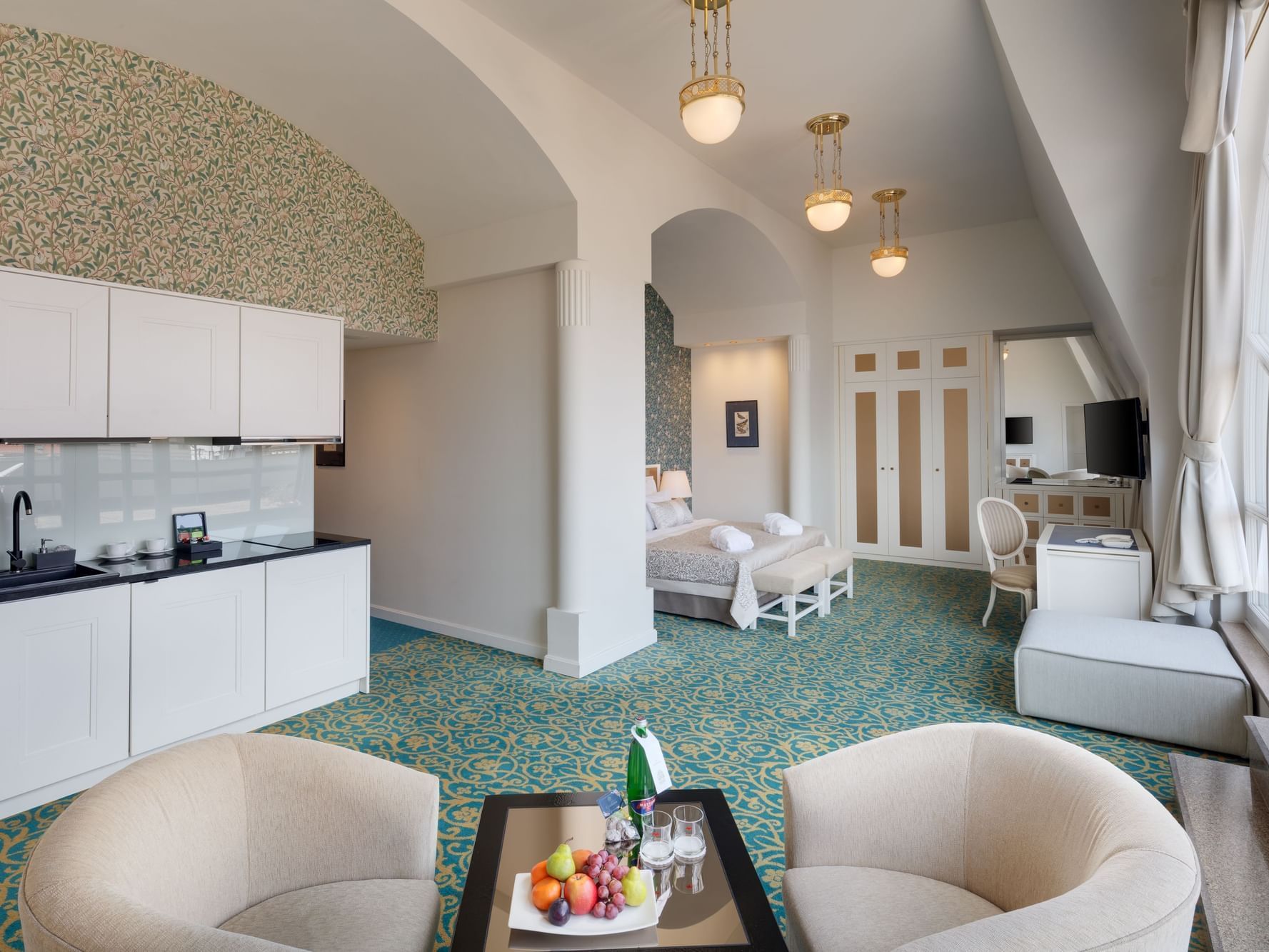 Elegant suite with sitting area, white kitchen, large bed and scenic terrace window view.