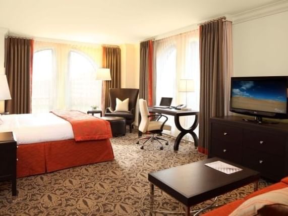 bed in carpeted hotel room facing television and windows