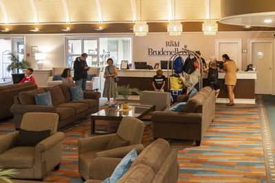 Guests standing by a registration counter in a spacious lobby with seating areas at Rodd Brudenell River Resort