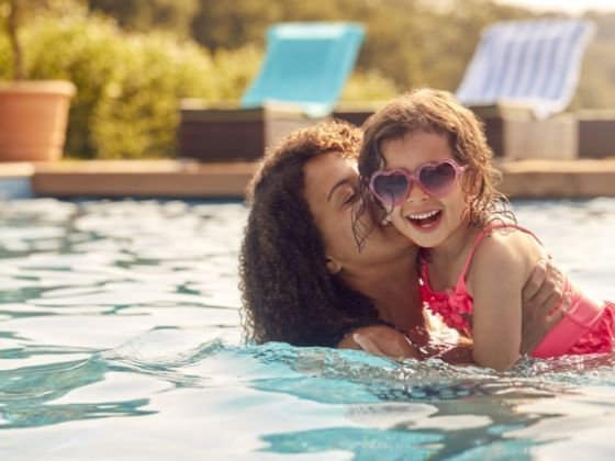 A mother holds her young, smiling daughter while swimming in a pool