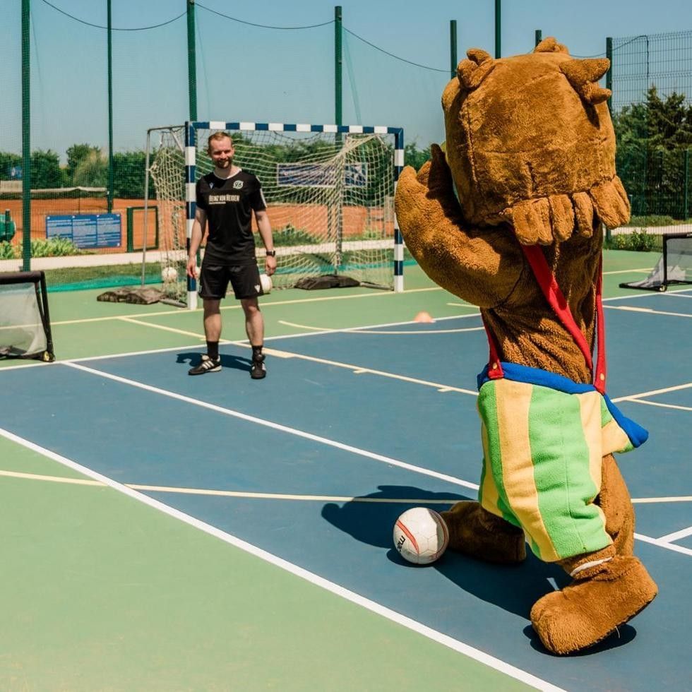 Mascot and man on sports court with soccer ball at Falkensteiner Family Resort Sicily