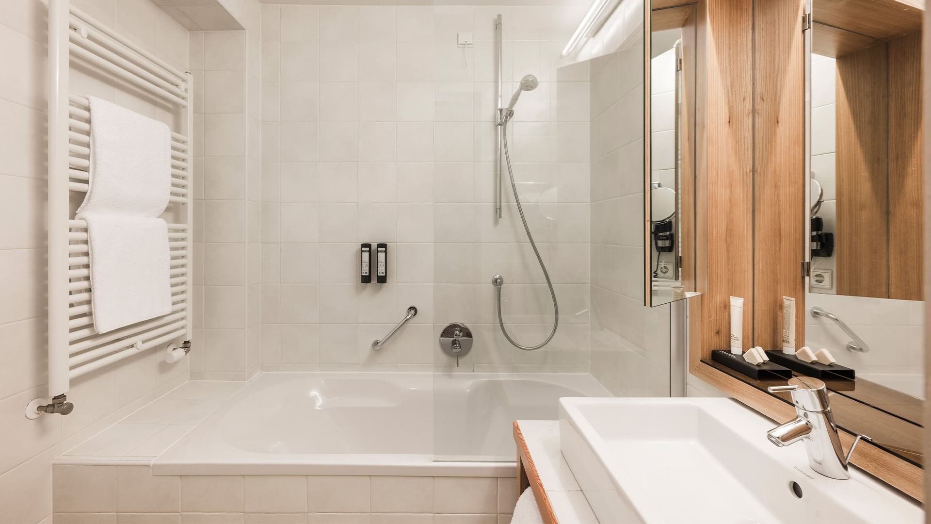 Bagno con vasca, doccia, asciugamani, specchio, lavabo e rubinetti.