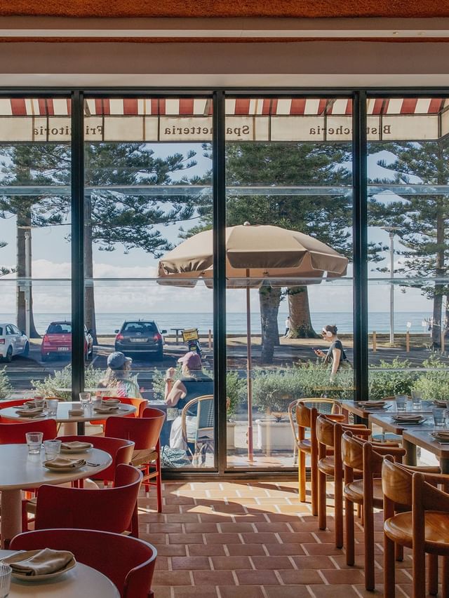 Chairs set by tables in a restaurant, looking through windows under striped awnings toward the sea at Elysium Manly