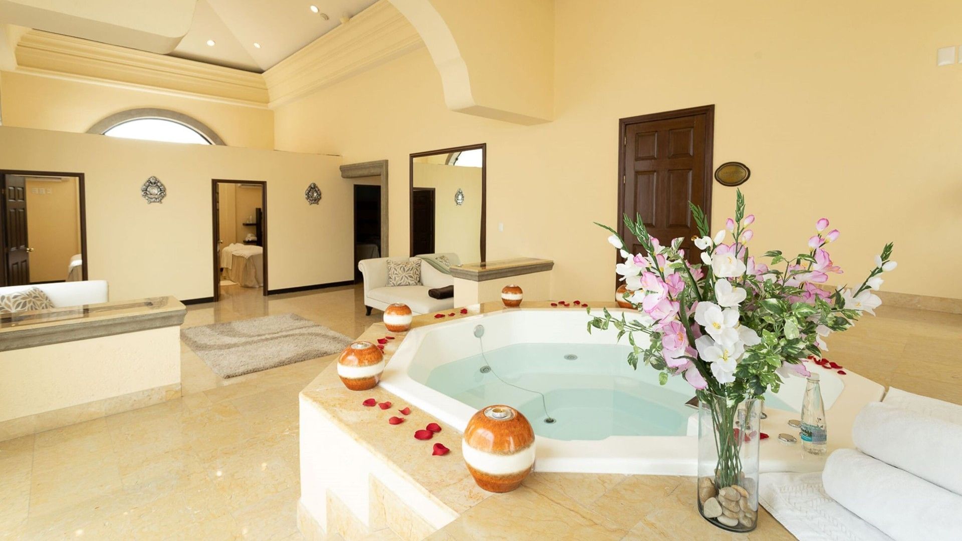 Octagonal whirlpool tub decorated with rose petals and a vase of pink lilies at Quinta Real Monterrey