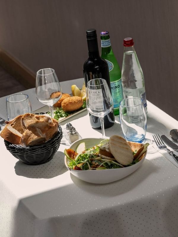 Table setting for one with bread in a basket placed by a salad near wine bottles at Warwick Grand Place Brussels